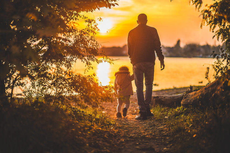 Grandparent holding hands with child and walking into sunset by the lake
