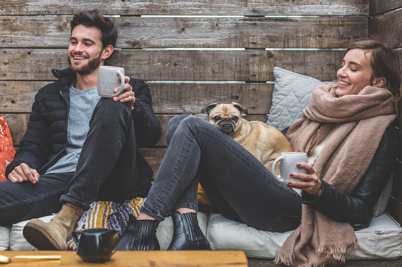 Couple sitting outside in their garden with a dog holding hot drinks