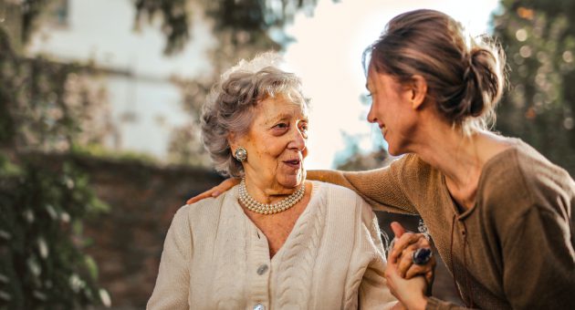 An elderly lady and a younger woman smiling at one another as they have funeral care cover