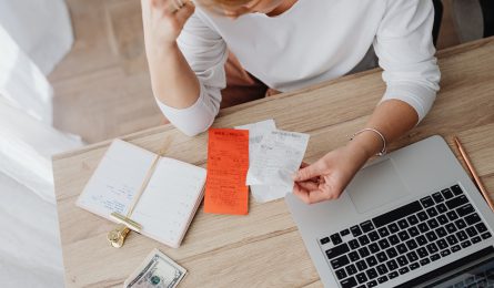 woman with her macbook looking at receipts and notes to improve her financial wellbeing